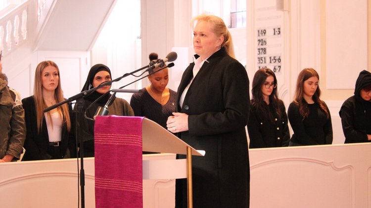 Eine Frau im schwarzen Mantel spricht in ein Mikrofon in einer Kirche.