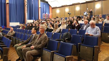 Schüler und Erwachsene sitzen in einer Aula. 
