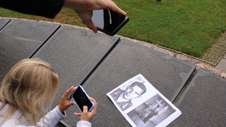 Zwei Personen fotografieren ein Schwarz-weiß-Foto eines Gefallenen, das auf einer Bronzetafel mit seinem Namen liegt.