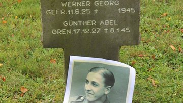 Ein Schwarz-weiß-Foto eines Gefallenen vor seinem Grabstein.
