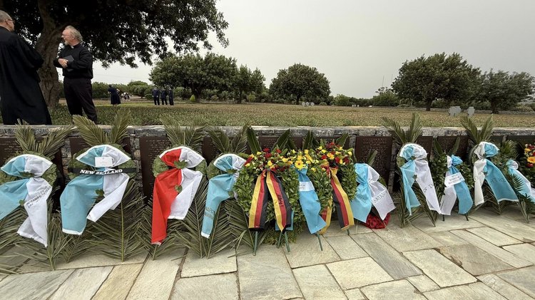 13 Kränze, unter anderem mit der deutschen Fahne, stehen an eine Mauer gelehnt.