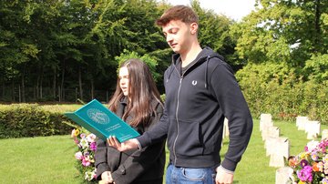 Zwei junge Menschen tragen etwas auf einer Kriegsgräberstätte vor. 