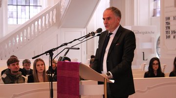 Ein Mann im Anzug spricht in einer Kirche am Mikrofon.