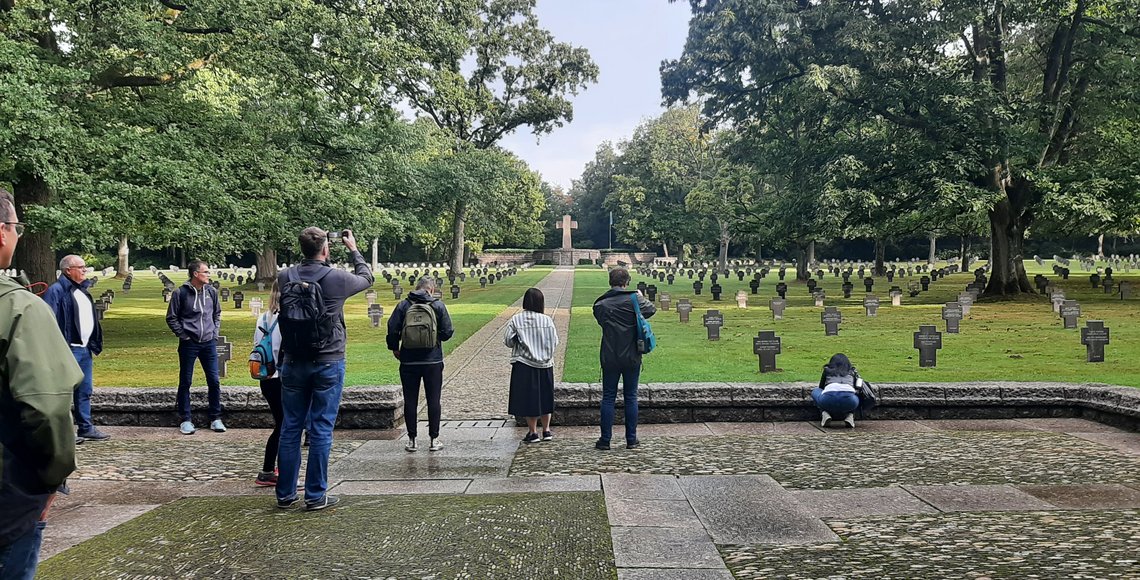Eine kleine Gruppe Menschen fotografiert eine Kriegsgräberstätte