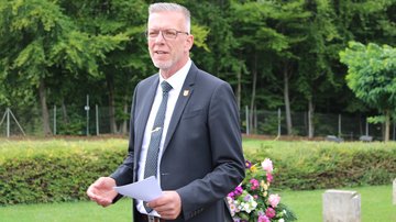 Ein Mann im Anzug spricht auf einem Friedhof. 