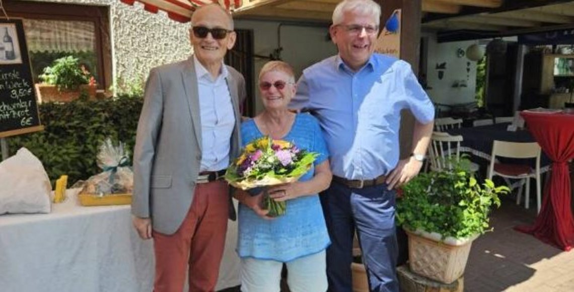 Eine Frau mit Blumenstrauß steht lachend zwischen zwei Männern.