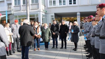 Soldaten und einige Zivilisten stehen zusammen, ein Mann trägt etwas vor.