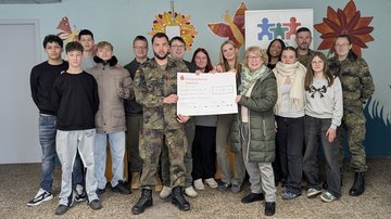 Schüler und Soldaten schauen in die Kamera und halten einen Scheck hoch.