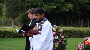 Zwei Geistliche tragen etwas auf einer Kriegsgräberstätte vor. 