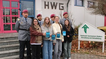 Vier Schülerinnen und vier Soldaten stehen vor einem Gebäude.