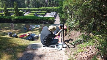 Zwei Männer arbeiten an einem Treppengeländer auf einem Friedhof