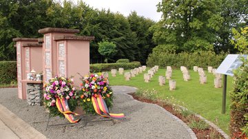 Eine Kriegsgräberstätte mit Infotafeln und Gedenkkränzen