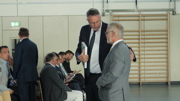 Ein Mann im Anzug legt einem anderen Mann im Anzug den Arm um die Schulter.