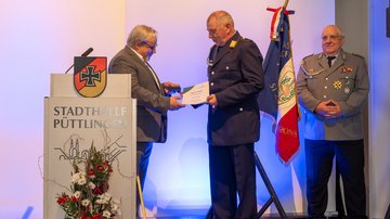 Ein Mann im Anzug verleiht ein Ehrenkreuz an einen Mann in Uniform